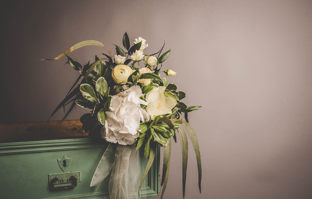 A beautiful bouquet of white roses and other flowers sits on an antique dresser in front of an off-white wall